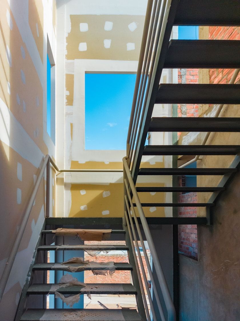 Stahltreppe in einem Rohbau, durch die Fensteröffnungen ist blauer Himmel zu sehen.