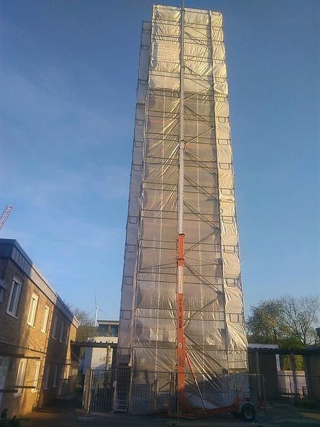 Hoher, vollständig mit Planen eingehauster Gerüstturm neben einem Wohngebäude.